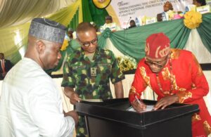 Director-General, National Youth Service Corps (NYSC), Brig.-Gen. Olakunle Nafiu (M); Retired Director of Audit, NYSC, Dr Levi Agim (R); signing his retirement certificate during the NYSC 2026 Batch B Pre- orientation workshop in Abuja on Tuesday (2/6/26). With them is the  Director, Special Duties Department, Mr George Mfongang./TUE/JUNE/2/2026/Deborah Bada/NAN 